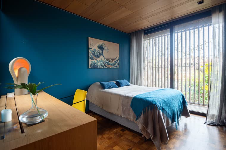 Dormitorio con pared azul, techo de madera y ventanal